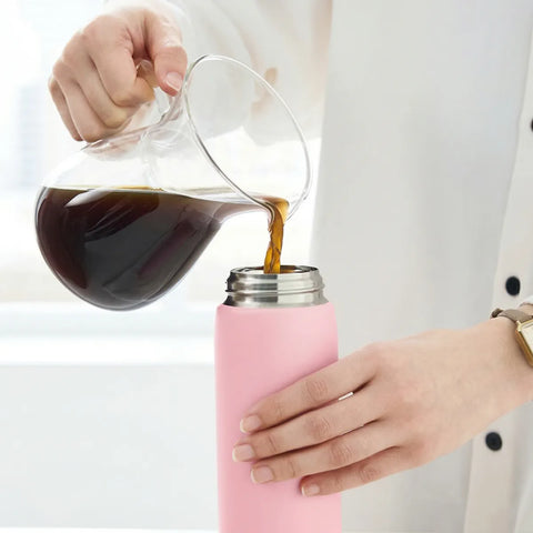 Person pouring coffee from a glass carafe into a pink thermos.