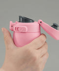 Hand holding a pink water bottle with black cap against a gray background