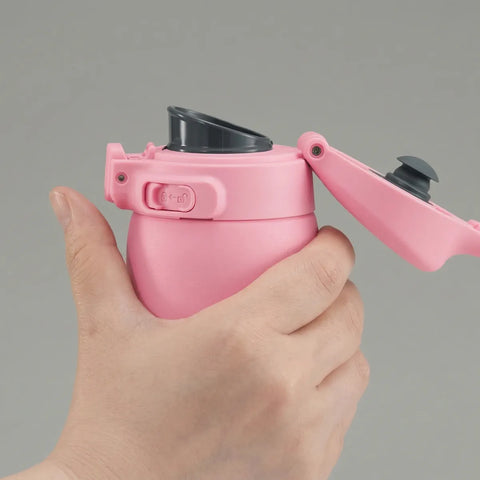 Hand holding a pink water bottle with black cap against a gray background