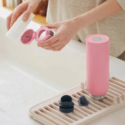 Person holding a pink bottle with a cap, next to a pink bottle on a drying rack.