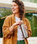 Woman in mustard jacket holding a silver water bottle outdoors
