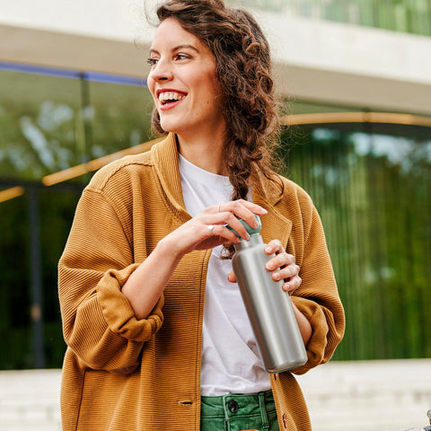 Woman in mustard jacket holding a silver water bottle outdoors