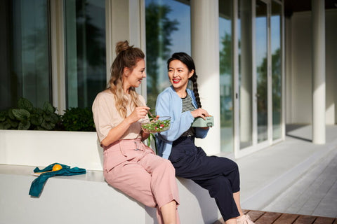 Two women sitting on a porch, enjoying a meal together.