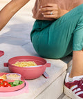 Person sitting on steps with a pink meal prep container and food items.